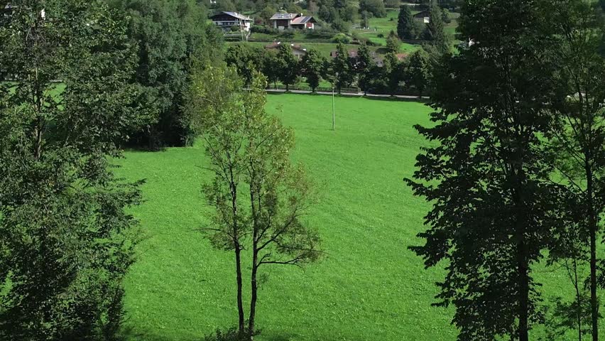 Aerial view of wide green fields and surrounding forested mountains near the village of Bezzecca in Valle di Ledro on a sunny day
