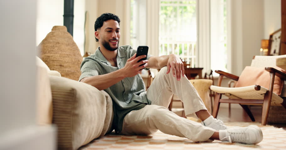 Video call, wave and man in house with phone, hello and online conversation in living room. Digital, happiness and male person on lounge floor with technology, kiss and connection on chat app.