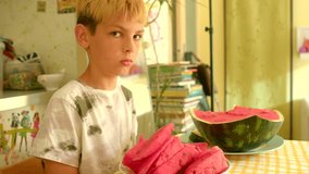 blond white boy eating watermelon slice at sunny kitchen table, pink cloth and stacked books in background, - Powered by Shutterstock - Get 15% off with code: PIKWIZARD15