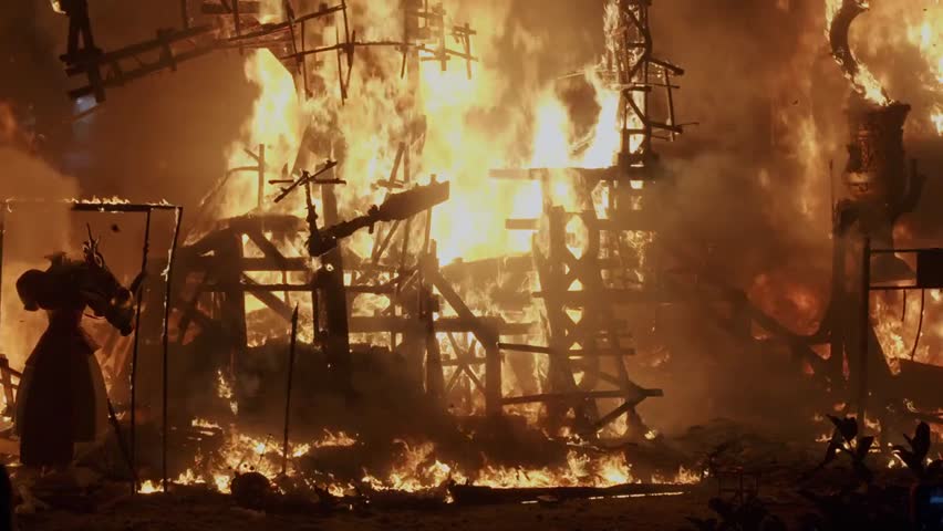 Bonfires burning on the streets of Valencia, Spain, creating a dramatic festive atmosphere with glowing flames, smoke, and lively cultural celebration at night.