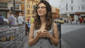 Woman holding mug on street under building facades in city center with glasses and gentle smile; serenity. - Powered by Shutterstock - Get 15% off with code: PIKWIZARD15
