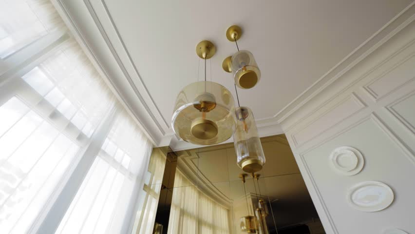 Modern transparent glass pendant lights with golden accents and warm bulbs in a bright contemporary interior with reflective glossy surfaces — elegant luxury lighting design element