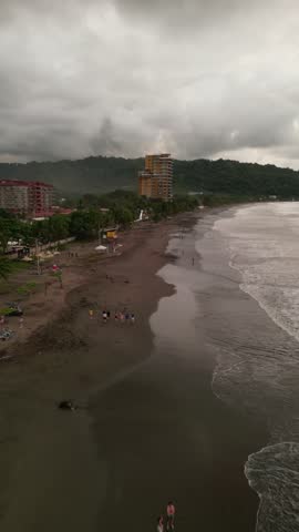 Vertical aerial view of the coastline with waves at sunset near the beach town of Jaco with tourist and hotel buildings and businesses on Jaco Beach located in the province of Puntarenas in Costa Rica