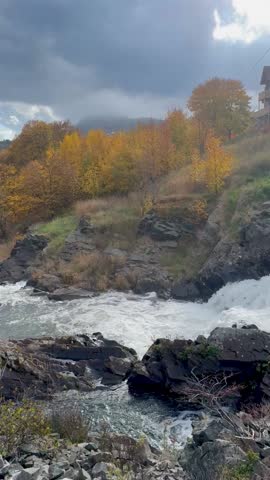 Mountain river running through a colorful autumn forest under a moody sky. Mist hides distant hills, creating a calm and dramatic scenery of the Canadian landscape.