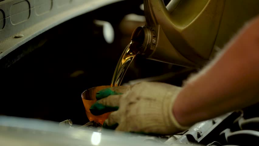 An auto mechanic pours new oil into an engine at a service center.
