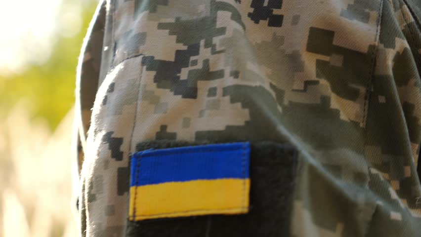 Close up of military blue-yellow chevron on shoulder of ukrainian soldier while going at countryside. This a powerful symbol of national identity, courage and unity. Concept of invasion resistance