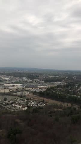 Ascending aircraft view of Manchester New Hampshire neighborhoods, wooded parcels, and commercial complexes under gray late-April cloud cover