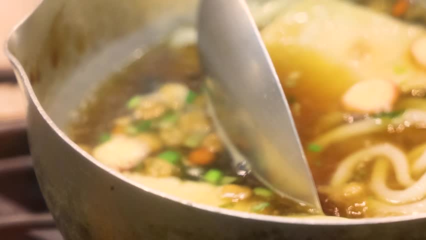 Bubbling Asian noodle soup in a pot with tofu and fish cubes along with vegetables captures vibrant street food scene on the streets of Asia showing rich flavors textures and hot savory atmosphere.