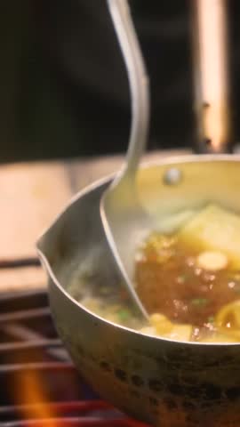 Bubbling Asian noodle soup in a pot with tofu and fish cubes along with vegetables captures vibrant street food scene on the streets of Asia showing rich flavors textures and hot savory atmosphere.