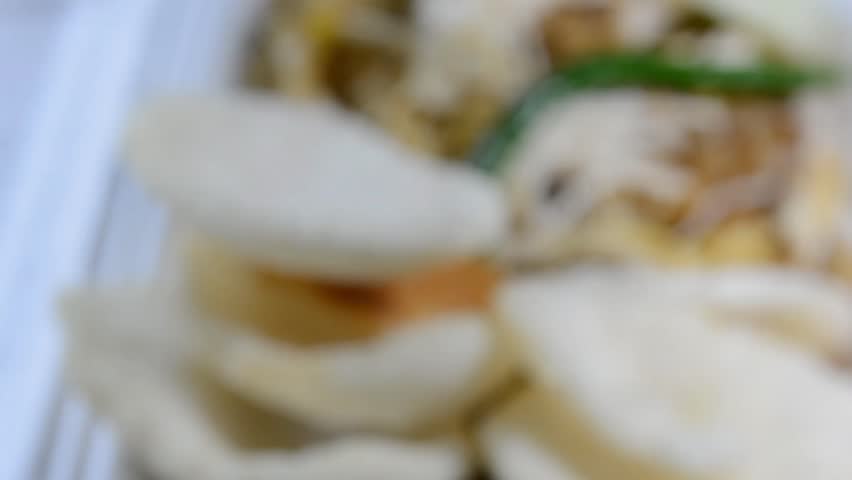 Close-up of Nasi Goreng Kampung (Indonesian fried rice) topped with shredded chicken (Ayam Suwir) and cucumber slices on a foam container