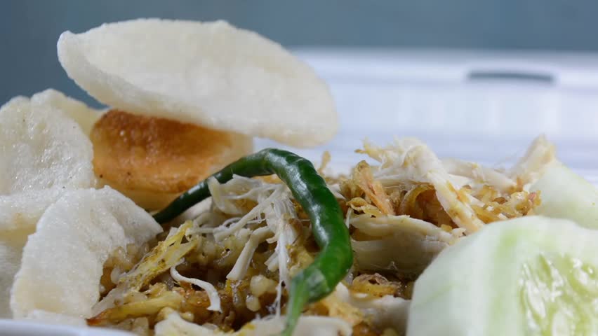 Close-up of Nasi Goreng Kampung (Indonesian fried rice) topped with shredded chicken (Ayam Suwir) and cucumber slices on a foam container