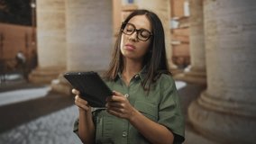 Woman brunette wearing glasses in green shirt reads a tablet with hand on neck near old town building columns and cobblestone street; confusion planning. - Powered by Shutterstock - Get 15% off with code: PIKWIZARD15