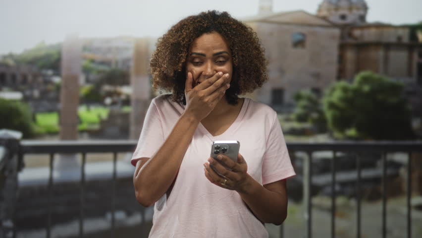 Woman holding smartphone, smiling and gesturing with open hand at building ruins balcony in rome; joy travel discovery.