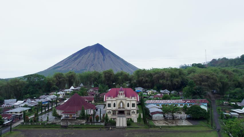 Establishing aerial footage of a village and church located in a tropical valley below the conical, majestic Mount Inerie, Flores, Indonesia.
