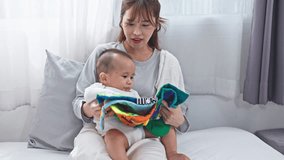 Asian mother baby infant reading cloth book parenting bonding indoor bedroom gentle moment as young mother reads colorful fabric book to baby bed sharing tender warm smile and joyful nurturing sofa - Powered by Shutterstock - Get 15% off with code: PIKWIZARD15
