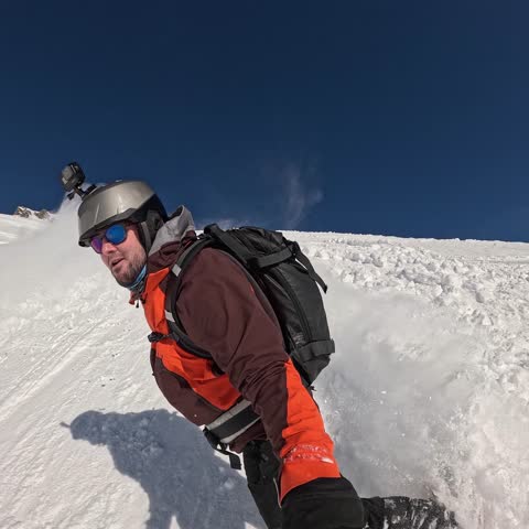 Candid, authentic selfie POV shot of an adventurous male snowboarder carving deep powder snow on a sunny day in the backcountry. Captures the thrill of the ride.