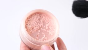 A close-up of a makeup brush scooping shimmering powder from a jar on a white background - Powered by Shutterstock - Get 15% off with code: PIKWIZARD15