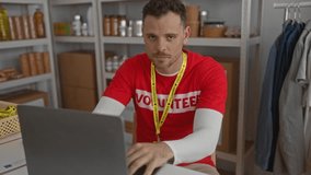Young man volunteering in a charity room working on a laptop surrounded by donations showing a volunteer badge and smiling. - Powered by Shutterstock - Get 15% off with code: PIKWIZARD15