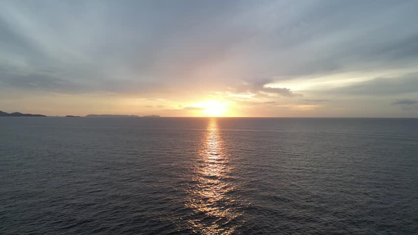 A drone view of a dramatic sunset over a dark ocean, with the sun