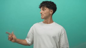Man pointing finger to left with right hand in teal studio wearing white t shirt and smirking, young hispanic casual pose; playful confidence. - Powered by Shutterstock - Get 15% off with code: PIKWIZARD15