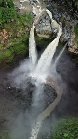 Stunning twin waterfall shot from above, surrounded by lush green jungle with dramatic water mist.