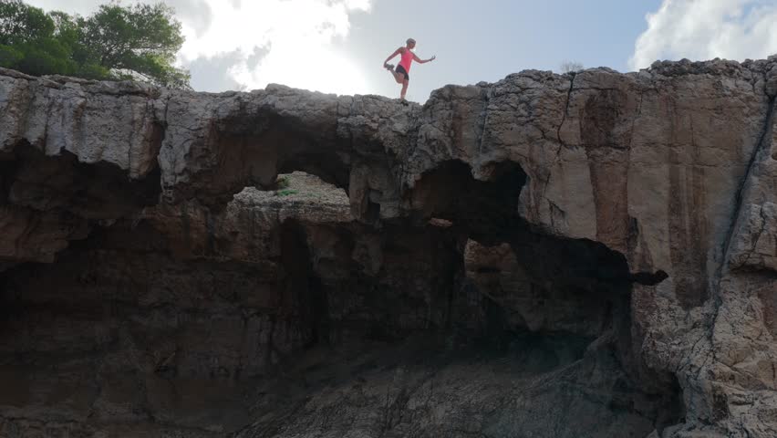 Adventurous Female Hiker Crossing the Dramatic Natural Stone Bridge at Cala d'Albarca in Wild Northern Ibiza