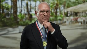 Senior man in suit with medal, standing thoughtfully on an outdoor street with blurred greenery, conveying business success and maturity. - Powered by Shutterstock - Get 15% off with code: PIKWIZARD15