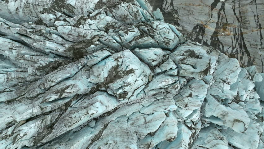 A top-down drone footage of the Argentiere Glacier revealing deep crevasses and blue ice layers mixed with rock debris in the French Alps