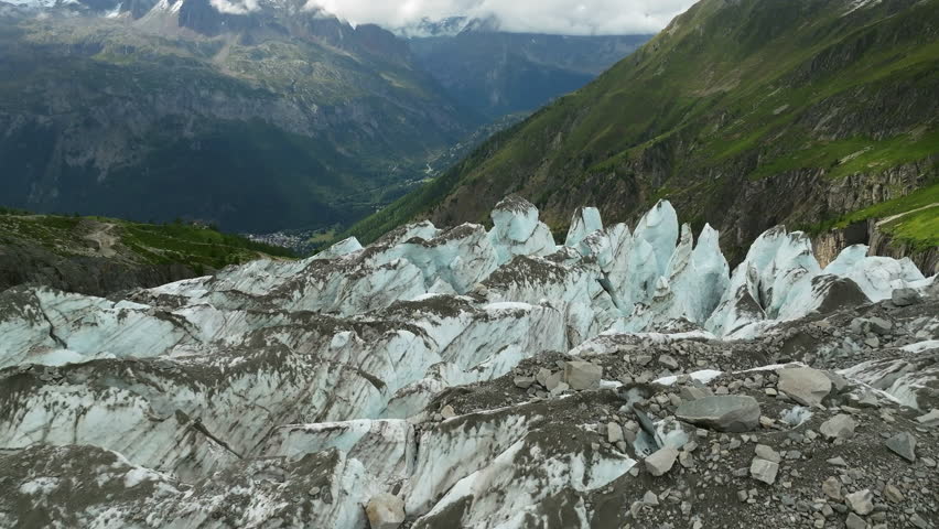 An aerial view of the upper Argentiere Glacier with sharp ice pinnacles overlooking green alpine valleys in the French Alps