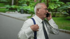 Senior man in suit talking on smartphone, smiling outdoors in lush green park environment, conveying business and communication themes. - Powered by Shutterstock - Get 15% off with code: PIKWIZARD15
