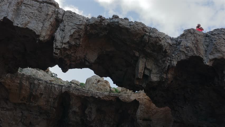 Adventurous Female Hiker Crossing the Dramatic Natural Stone Bridge at Cala d'Albarca in Wild Northern Ibiza