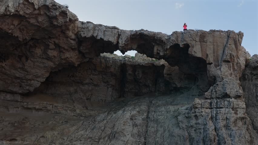 Adventurous Female Hiker Crossing the Dramatic Natural Stone Bridge at Cala d'Albarca in Wild Northern Ibiza
