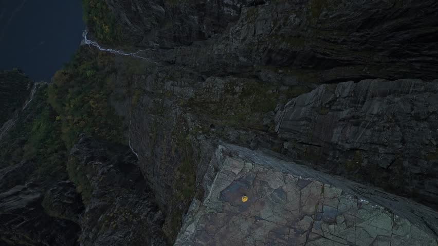 Sunset aerial view of solitary figure standing on iconic cliff, Norway