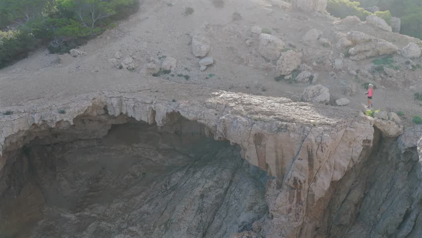 Adventurous Female Hiker Crossing the Dramatic Natural Stone Bridge at Cala d'Albarca in Wild Northern Ibiza
