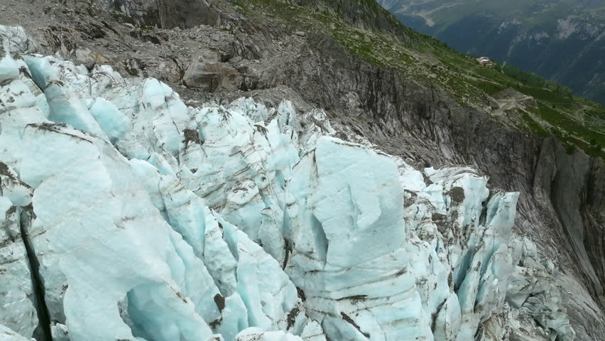 A close-up drone footage of blue ice formations and rocky edges of the Argentiere Glacier high in the French Alps