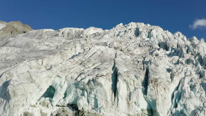 A pull-back drone shot of the rugged ice formations of the Moiry Glacier in Valais, Switzerland, under a clear blue alpine sky