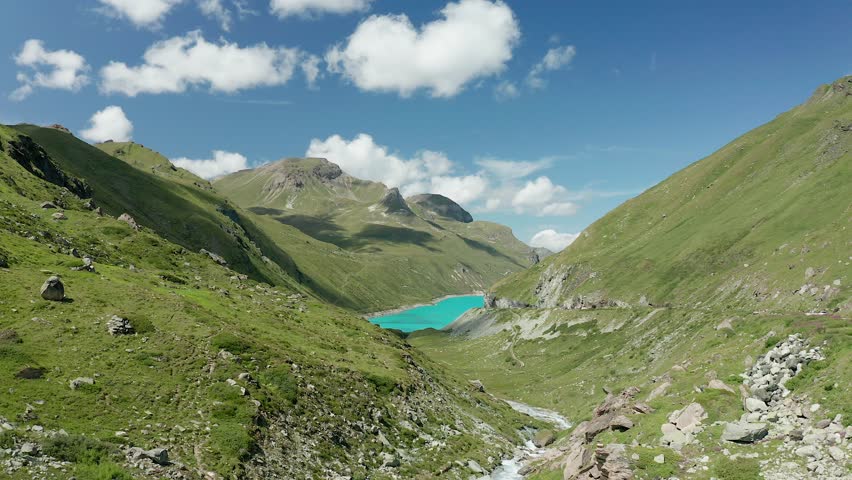 A drone shot of Moiry Lake (Lac de Moiry) surrounded by lush green hills and mountains in Valais, Switzerland, under a clear blue alpine sky