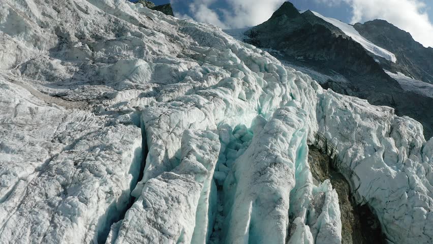 A close aerial view of the Moiry Glacier in Switzerland, showing tall ice spires and deep blue cracks, displaying natural beauty and signs of melting
