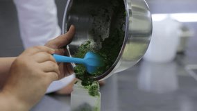 A chef carefully transfers vibrant green pesto from a stainless steel bowl into a clear bottle using a blue spatula.  - Powered by Shutterstock - Get 15% off with code: PIKWIZARD15