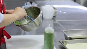 A chef carefully transfers vibrant green pesto from a stainless steel bowl into a clear bottle using a blue spatula.  - Powered by Shutterstock - Get 15% off with code: PIKWIZARD15