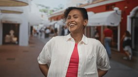 Woman smiling with hands on hips showing teeth on a busy shopping street with storefront awnings; joy community resilience. - Powered by Shutterstock - Get 15% off with code: PIKWIZARD15