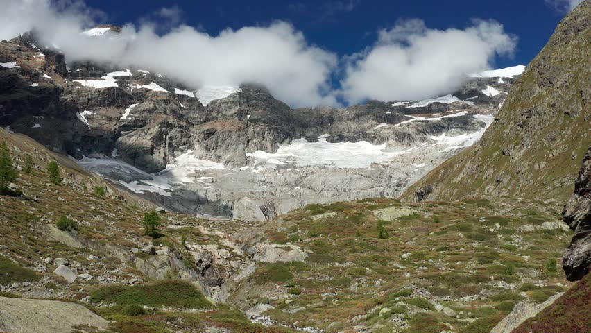 An aerial view of a distant Swiss glacier surrounded by alpine meadows and steep mountain slopes, showing visible melting and climate-driven retreat