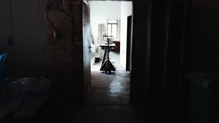 Older worker walking through dim workshop corridor and moving a loaded pallet jack during renovation — manual labor and small business scene