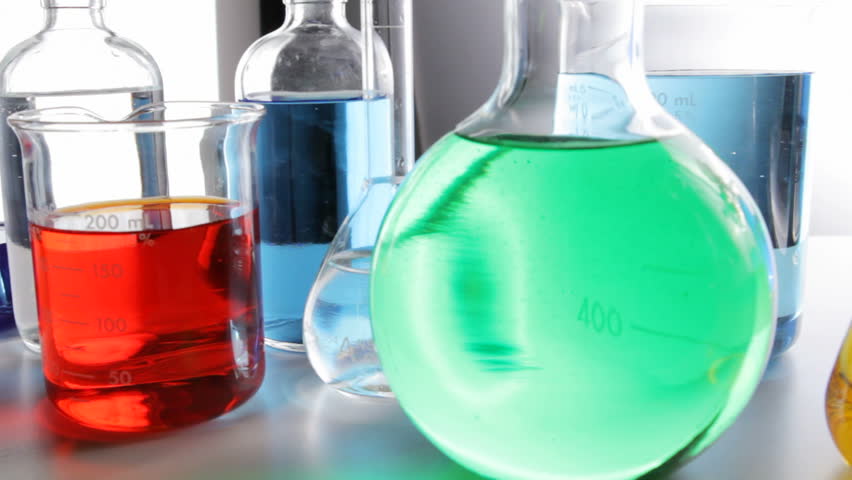 Camera pans along beakers, flasks and bottles filled with colorful chemicals