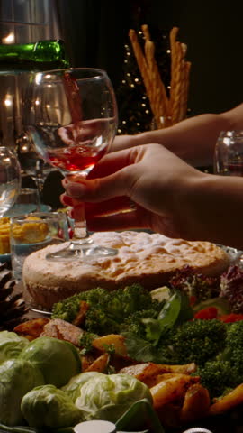Vertical slow motion video camera moving over festive dinner table hands serving salad pouring wine warm light cozy atmosphere thanksgiving or christmas celebration gratitude togetherness