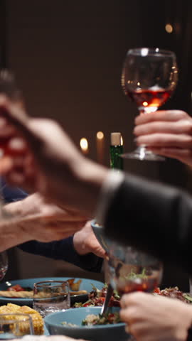 Vertical slow motion video camera gliding over festive table people clinking glasses of red wine cozy warm light holiday dinner thanksgiving or christmas family gathering gratitude joy togetherness
