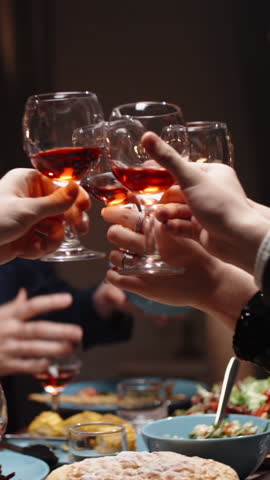 Vertical slow motion video camera gliding over festive table people clinking glasses of red wine cozy warm light holiday dinner thanksgiving or christmas family gathering gratitude joy togetherness