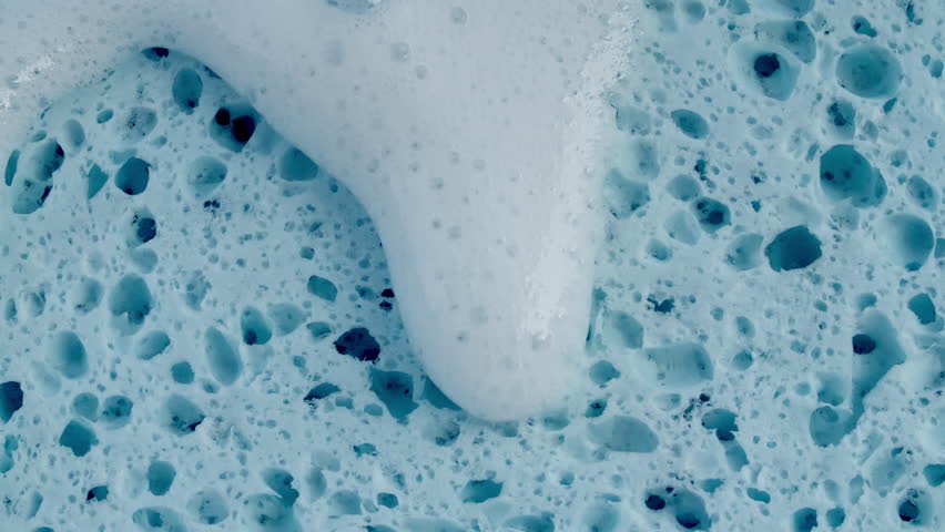 Bubbles of white soap foam. Moving Soap foam popping bubble on a blue backdrop. Soap sud macro structure. Clean, cleaning concept, laundry, shower. 