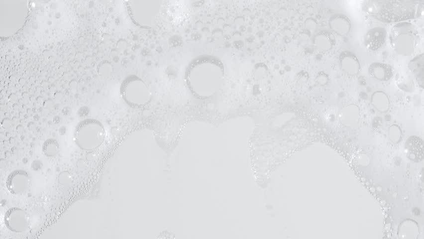 Bubbles of white soap foam. Moving Soap foam popping bubble on a white backdrop. Soap sud macro structure. Clean, cleaning concept, laundry, shower. 