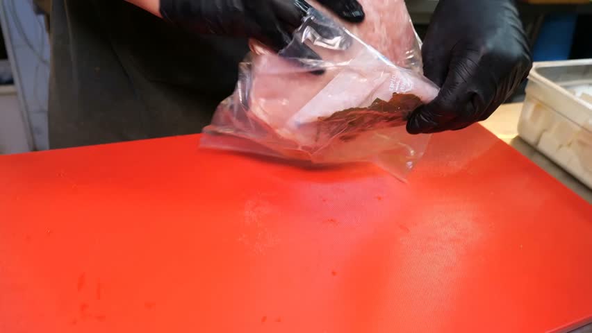 A professional chef wearing black gloves taking boneless pork or chicken cutlets, and placing thick pieces of cheese on each cutlet to roll them into savory meat and cheese rolls